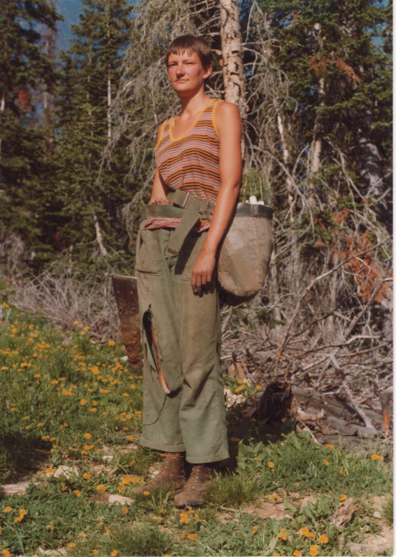 Tree planter Jane Feetch poses with pickaxe and bag of saplings against a forest backdrop.